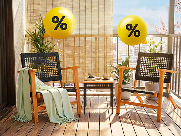 屋外バルコニーに、ウィッカー製の椅子2脚とテーブルを配置したアウトドア家具のシーン。パーセント記号が描かれた黄色いバルーンが飾られています。クリックするとコレクション内の商品をご覧いただけます。