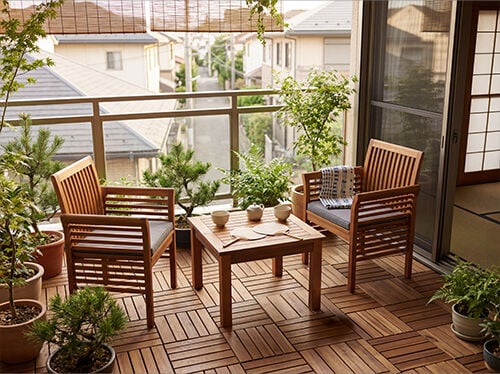 木製のバルコニーにはテーブルと椅子が2脚あり、鉢植えの植物に囲まれていて、住宅街を望む居心地の良い屋外リビングスペースを作り出しています。コレクション内の商品を見るにはクリックしてください。