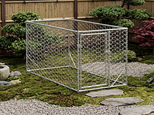 庭の砂利の上に置かれた、ワイヤーメッシュの側面を持つ亜鉛メッキ鋼製の犬用ケージ。背景には緑の低木と盆栽があります。コレクションの製品を見るにはクリックしてください。