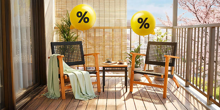 屋外バルコニーに、ウィッカー製の椅子2脚とテーブルを配置したアウトドア家具のシーン。パーセント記号が描かれた黄色いバルーンが飾られています。クリックするとコレクション内の商品をご覧いただけます。
