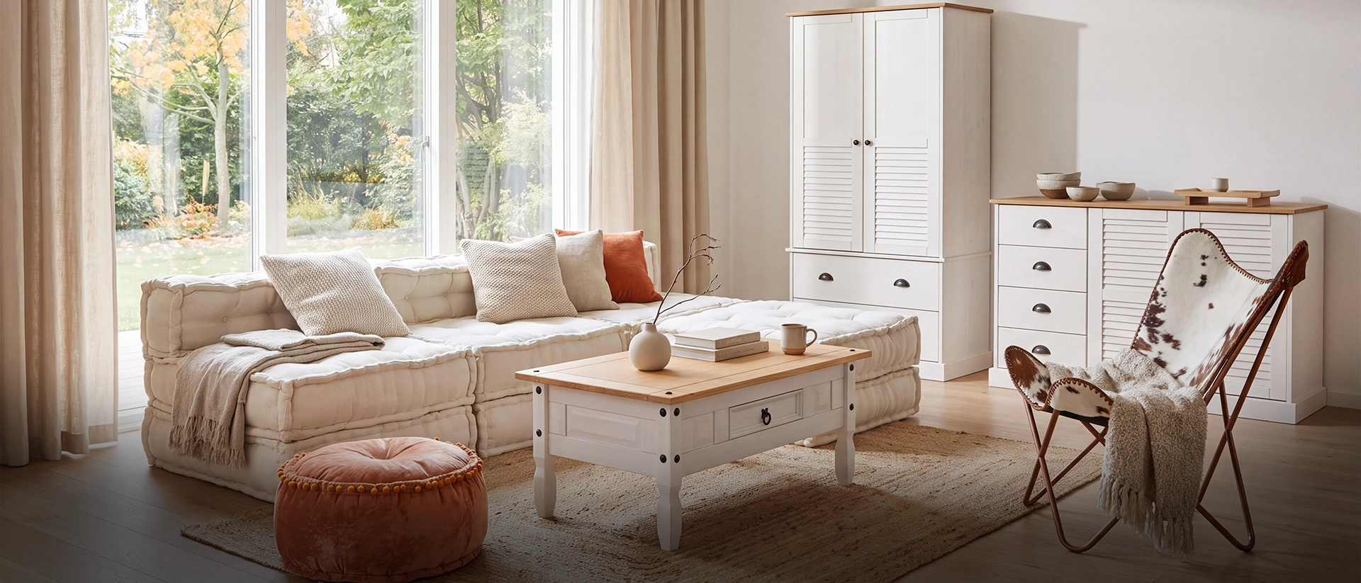 Bright living room with a beige tufted sofa, orange pillows, a wooden coffee table, a pink velvet pouf, white storage cabinets, and a cowhide butterfly chair.